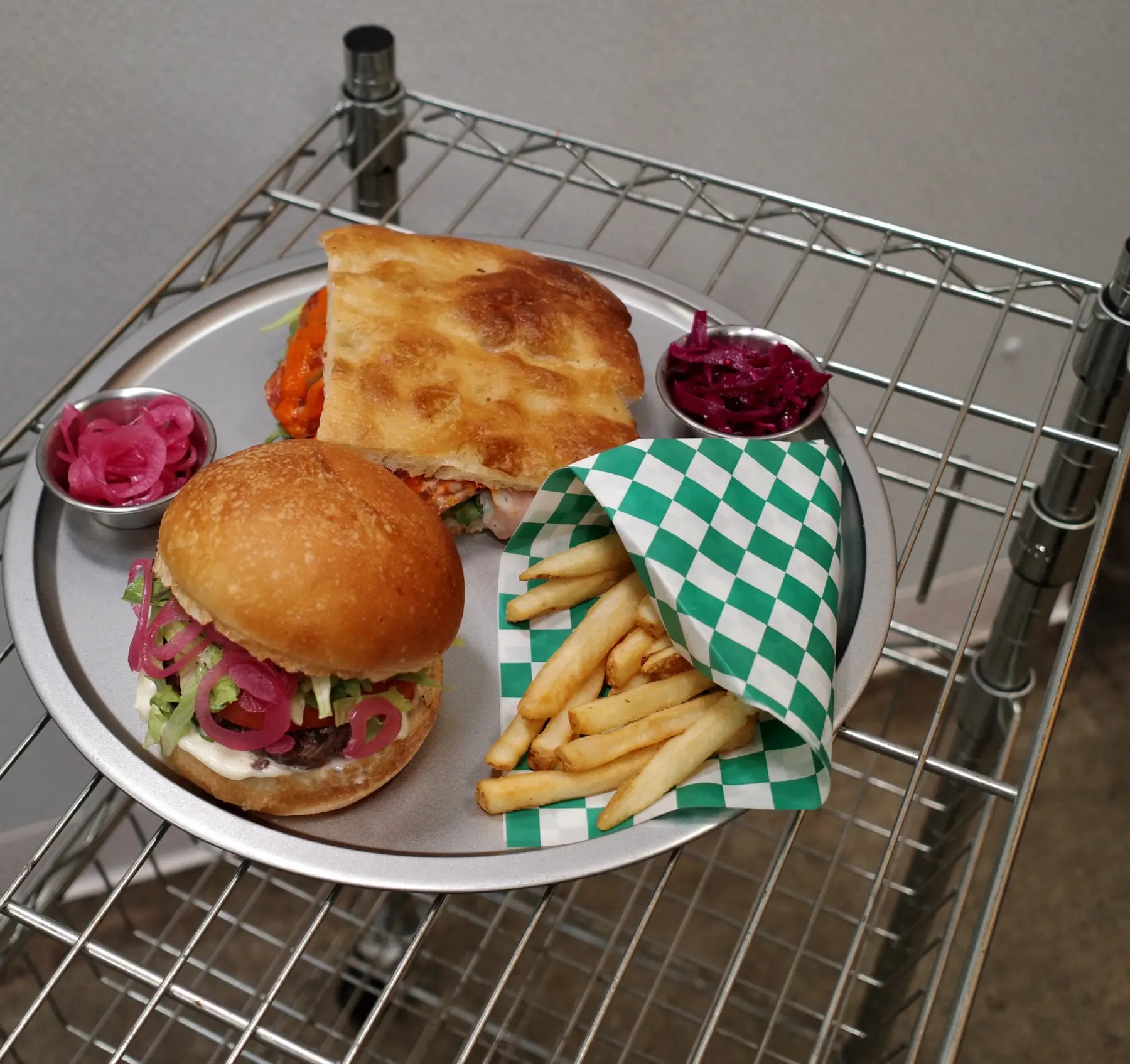 A focaccia sandwich, a burger with pickled red onion and fries on a tray